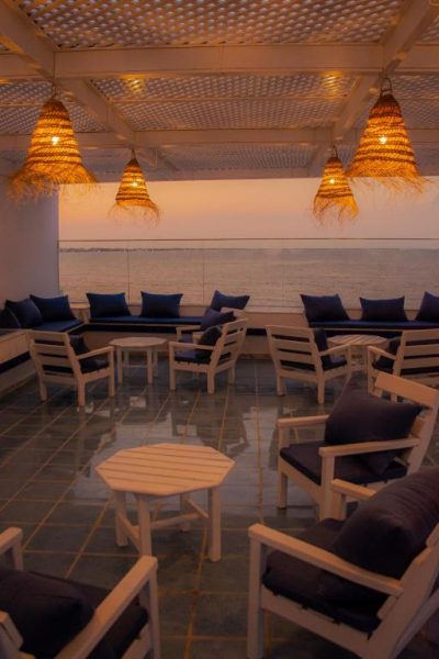 Terraza lounge con sillones blancos y cojines azules con vistas al mar al atardecer en Hôtel Al Jazira Mahdia