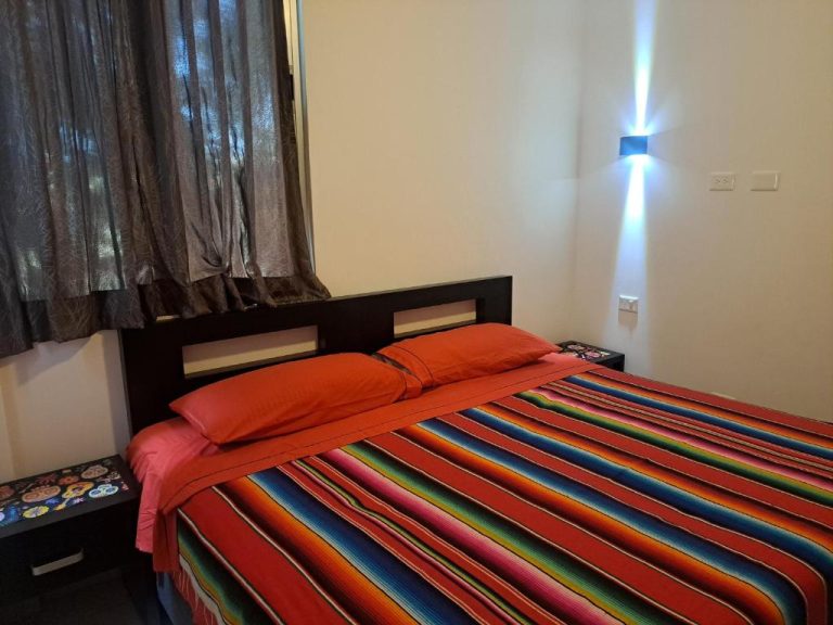 Habitación con cama matrimonial y colcha multicolor en Condo Kiaraluna, decoración moderna con iluminación azul