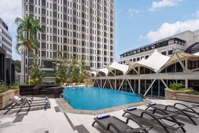 Piscina exterior con tumbonas y hamacas en la terraza del Wyndham Singapore Hotel con vistas a la torre