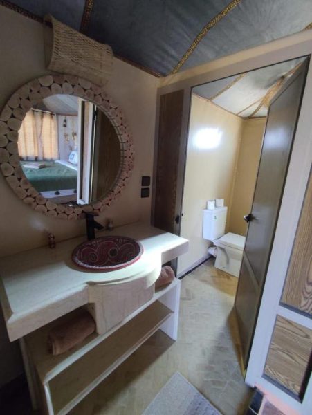 Baño con lavabo artesanal y espejo redondo de madera en Velaria Luxury Camp