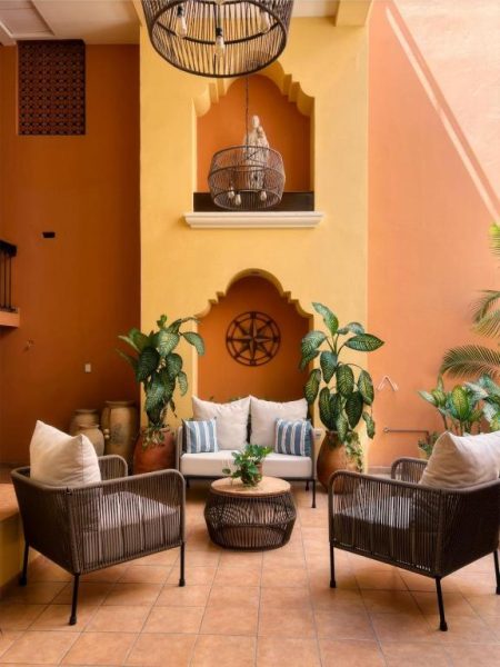 Terraza interior estilo colonial con sillones y sofá del Hotel Colli, decoración tropical y paredes ocre