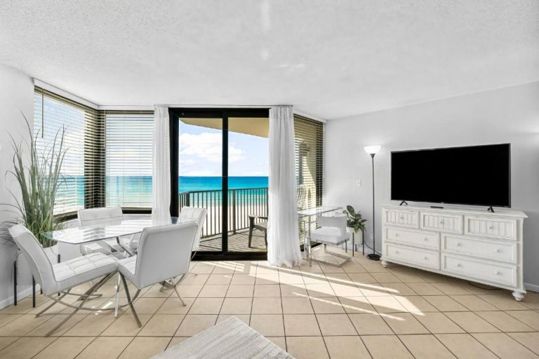 Salón con mesa de comedor, TV y balcón con vistas al mar turquesa en Sunbird of Panama City Beach