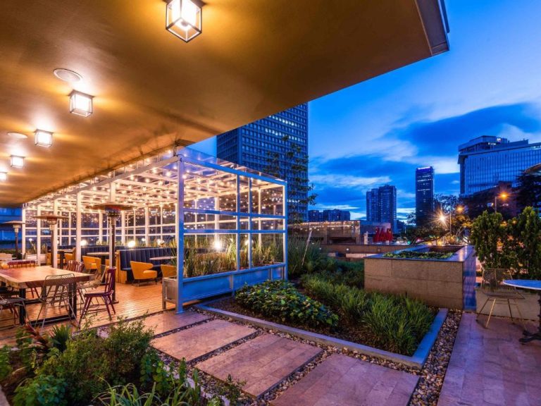 Terraza bar restaurante del ibis Bogotá Museo con jardín, iluminación nocturna y vista al skyline de la ciudad