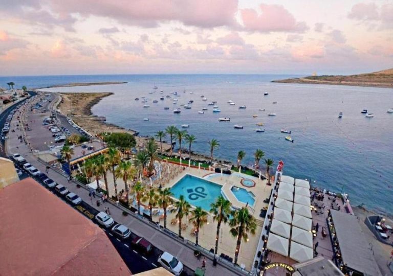 Vista aérea de la piscina exterior y zona de playa del Qawra Palace Resort & Spa en Malta