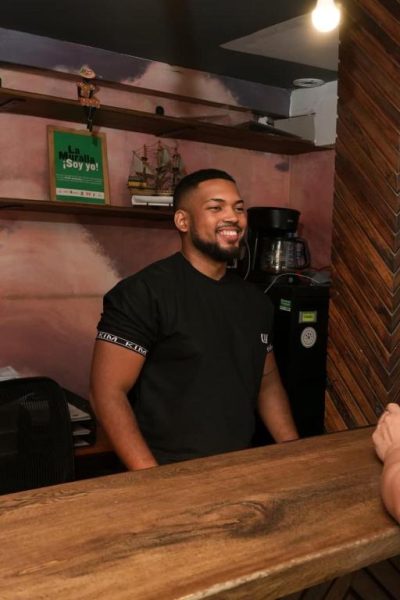 Recepcionista sonriente atendiendo en el mostrador del bar del Hotel Kim con cafetera al fondo