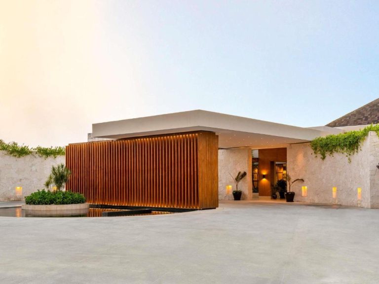 Entrada principal del Fairmont Mayakoba con diseño moderno, paredes de piedra y panel de madera iluminado