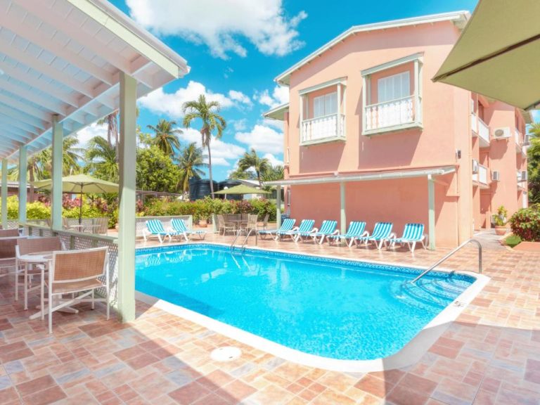 Piscina exterior con tumbonas azules y edificio rosa del Worthing Court Apartment Hotel en Barbados