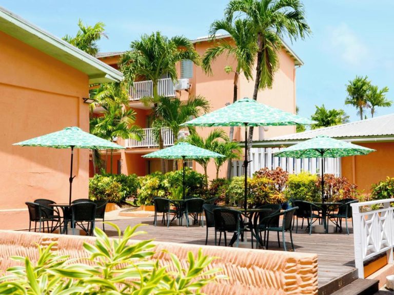 Terraza exterior con mesas y sombrillas del Worthing Court Apartment Hotel rodeada de palmeras tropicales