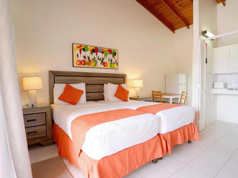 Habitación doble con camas en tonos naranja y cocina equipada en Worthing Court Apartment Hotel