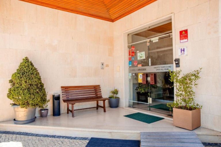 Entrada principal del Hotel Larverde con banco de madera, plantas decorativas y puerta de cristal automática