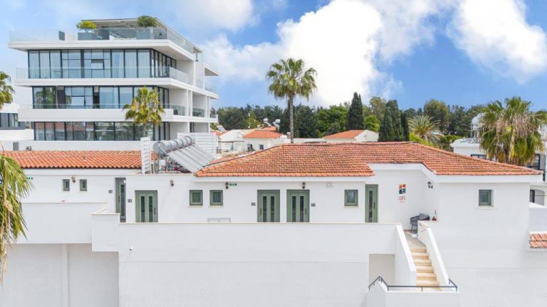 Fachada exterior blanca con tejado rojo del Loft Centrale rodeado de palmeras y edificio moderno al fondo