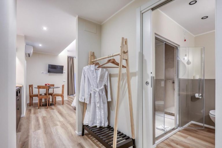 Baño con ducha de cristal y albornoz blanco en el pasillo del WelcHome Wellness Suites