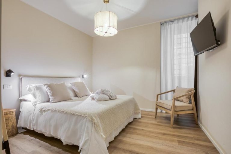 Habitación doble luminosa con cama blanca, suelo de madera y TV en WelcHome Wellness Suites