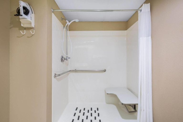 Baño accesible con ducha adaptada, barras de apoyo y asiento en Days Inn & Suites by Wyndham Cuba