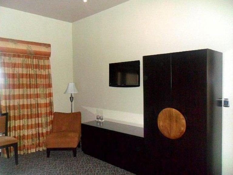 Habitación con armario oscuro, televisión de pantalla plana y sillón en Hotel 1915 Inn & Suites