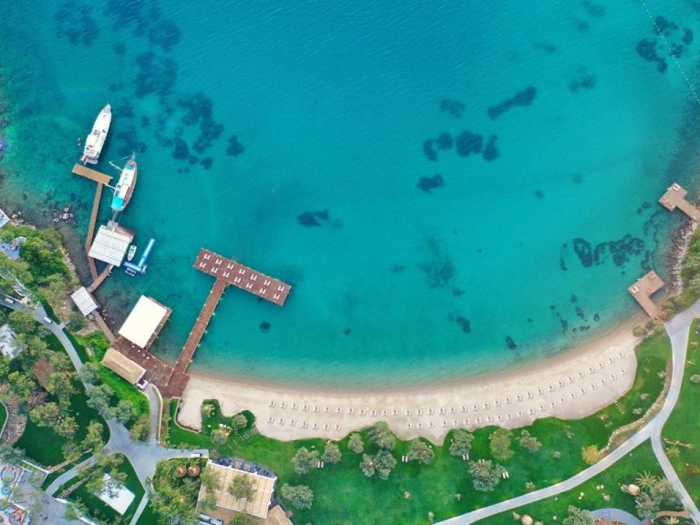 Vista aérea de la playa privada y muelle del Rixos Premium Bodrum con aguas turquesas