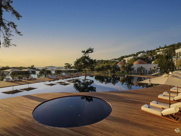 Piscina infinity con terraza de madera y tumbonas al atardecer en Rixos Premium Bodrum