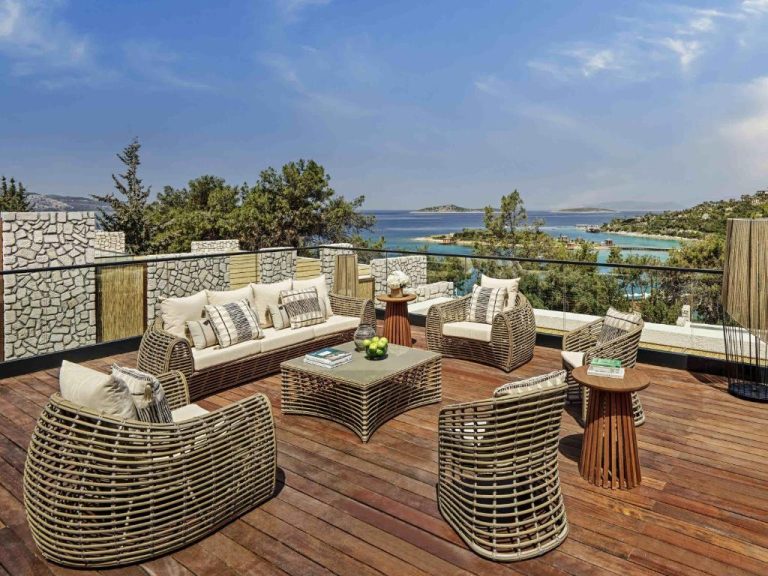Terraza con sofás de ratán y vistas al mar turquesa en Rixos Premium Bodrum