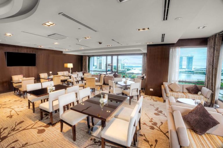 Salón Club Lounge del Wyndham Singapore con mesas, sofás y vistas panorámicas a Marina Bay