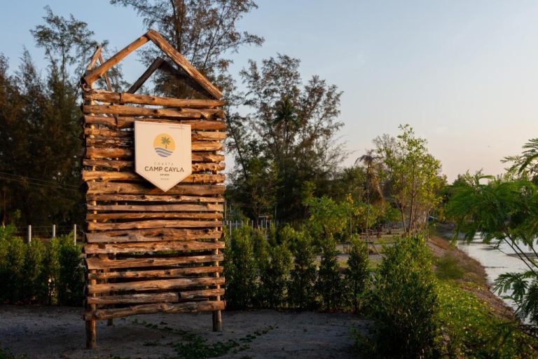 Cartel de entrada de madera rústica del Camp Cayla COASTA rodeado de vegetación junto al río