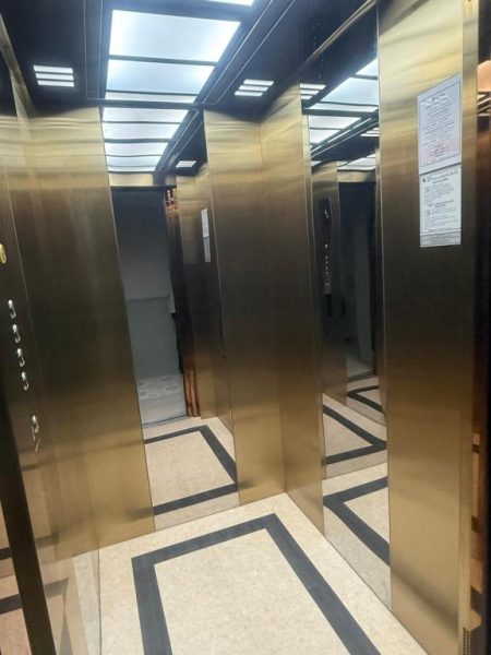 Ascensor moderno con paredes de acero dorado y espejos en el TUAN Hotel Bangkok cerca de Wat Arun