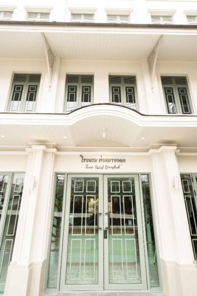 Fachada blanca y entrada principal del TUAN Hotel Bangkok cerca de Wat Arun, con puertas de cristal