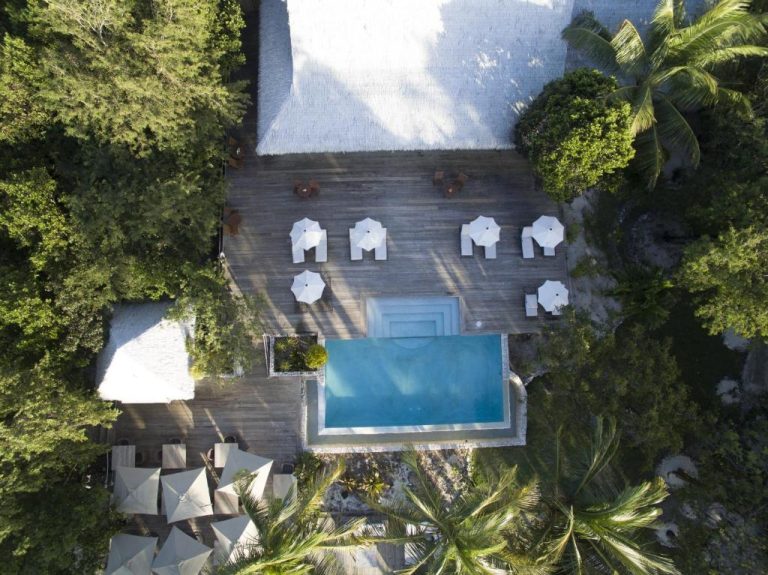 Vista aérea de la piscina exterior con terraza de madera y sombrillas del Tiamo Resort rodeado de vegetación tropical