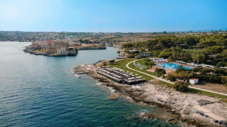 Vista aérea del resort Mangia's Brucoli Sicily con piscina exterior y tumbonas frente al mar en Sicilia