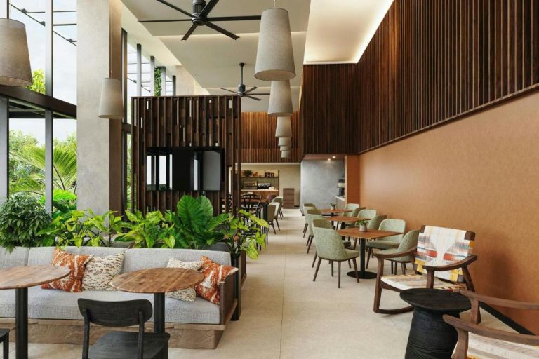 Lobby lounge con sofás, plantas tropicales y zona de restaurante en Residence Inn Marriott El Coyol