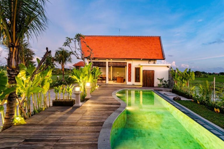 Piscina exterior iluminada con pasarela de madera y jardín tropical en Svadarma Bali Villa