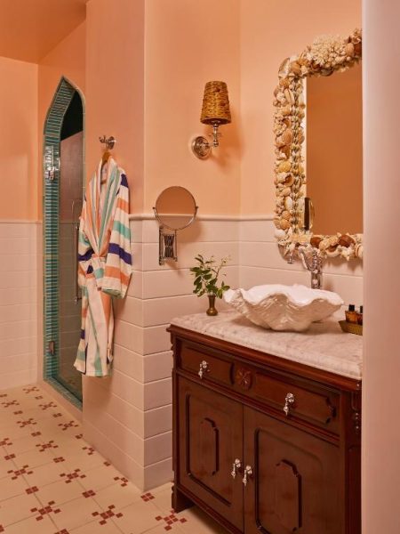 Baño decorado con lavabo en forma de concha y espejo enmarcado en conchas marinas del Coral Sands Inn