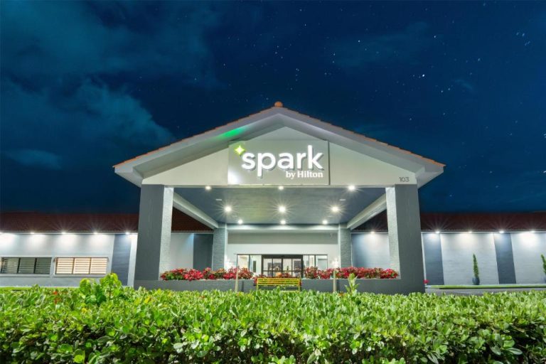 Fachada exterior iluminada del Spark by Hilton Ponce durante la noche con jardines y entrada principal