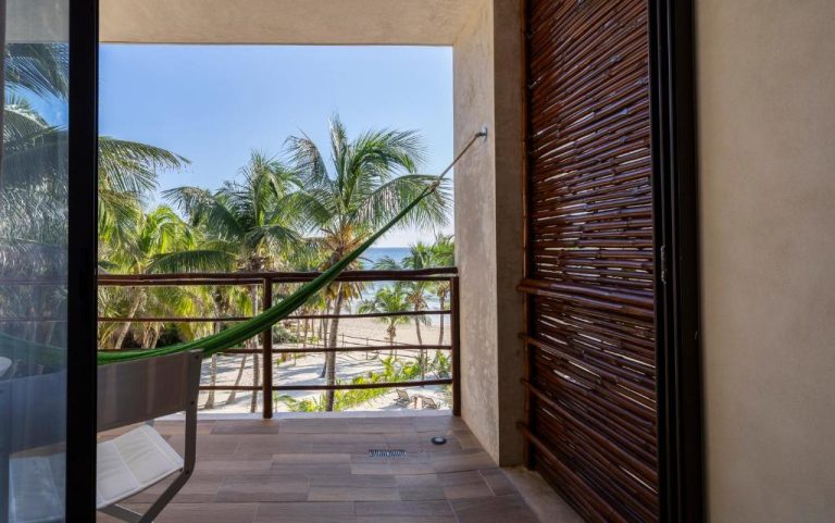 Balcón con hamaca y vista a la playa de palmeras en Hotel Los Arrecifes