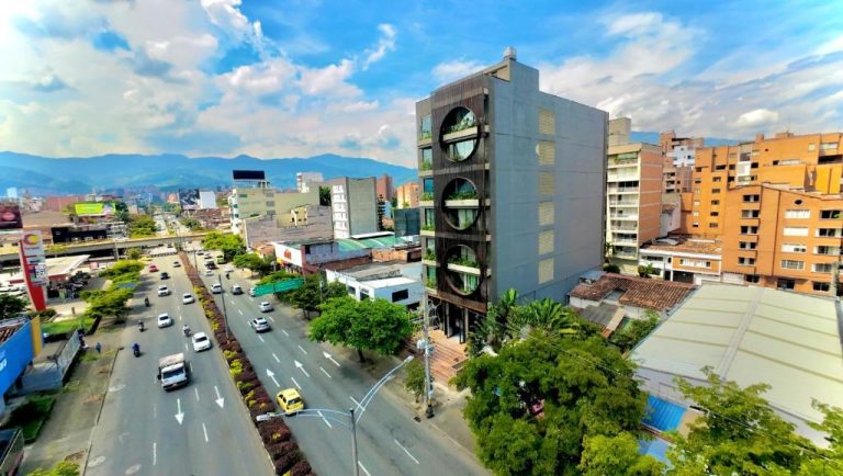 Vista aérea de la fachada exterior del Iconik Hotel con ventanas circulares y avenida principal de Medellín
