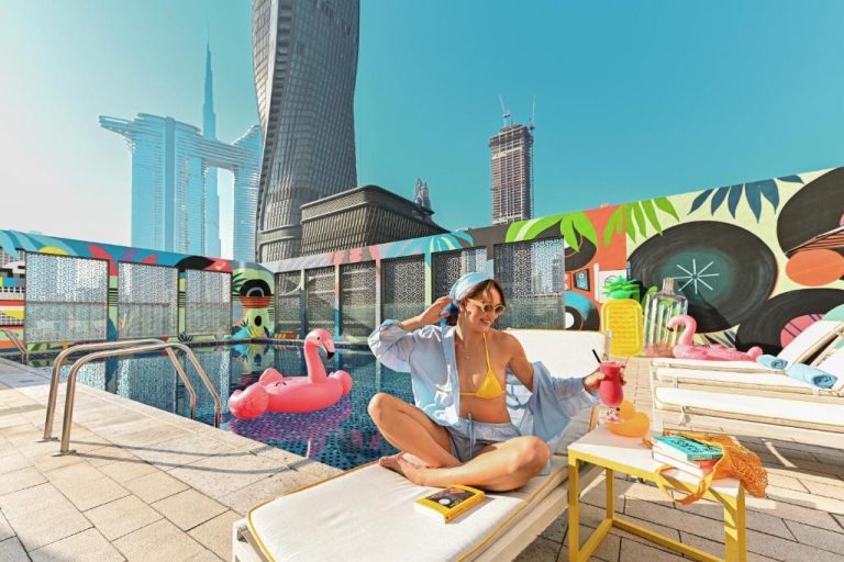 Mujer relajándose junto a la piscina en terraza del Rove City Walk con vistas al skyline de Dubái