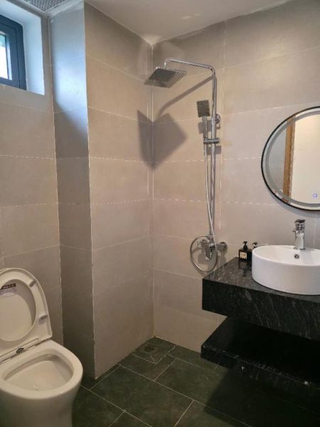 Baño moderno con ducha de lluvia, lavabo sobre encimera de mármol y espejo redondo en Huỳnh Nga Măng Đen Hotel