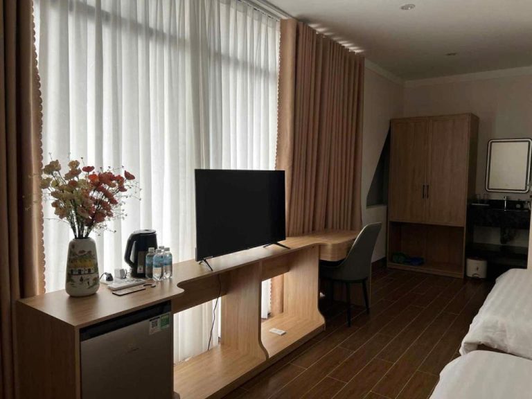 Habitación moderna con escritorio de madera, televisión y armario del Huỳnh Nga Măng Đen Hotel