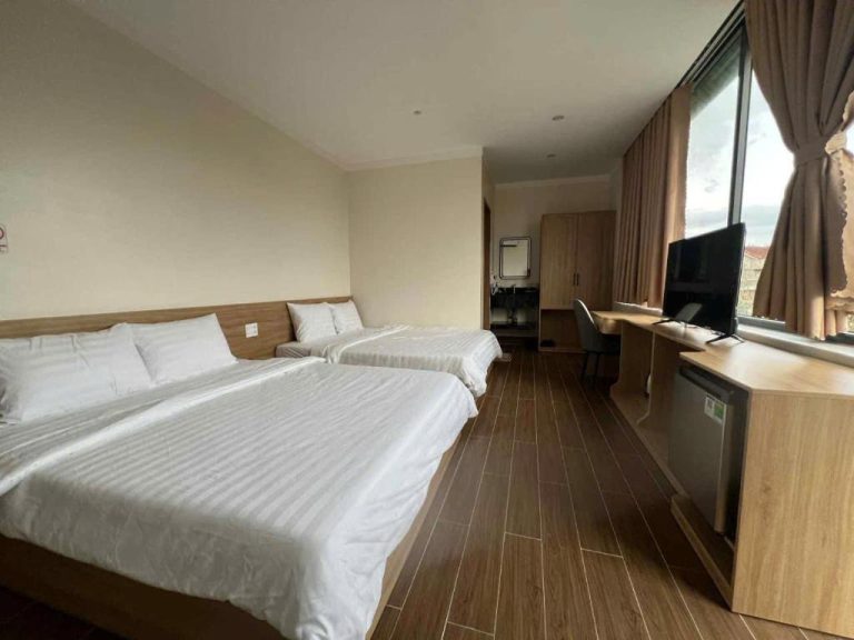 Habitación doble con dos camas y escritorio con televisión en Huỳnh Nga Măng Đen Hotel