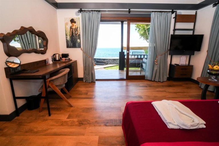 Habitación con cama roja, escritorio y vistas al mar desde terraza en Porto Amore Club Hotel