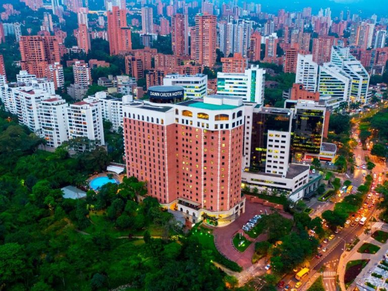 Vista aérea del Hotel Dann Carlton Medellín rodeado de vegetación y el skyline de la ciudad al atardecer