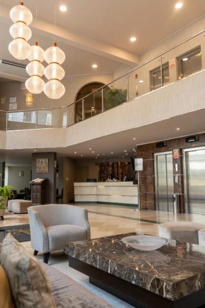 Elegante lobby con recepción, sofás grises y lámparas decorativas del Hotel Jose Antonio
