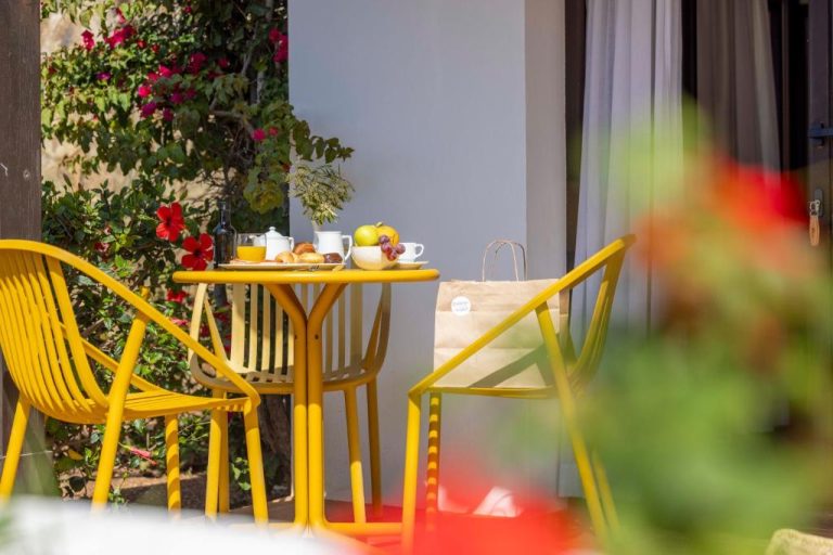 Terraza con mesa y sillas amarillas con desayuno en el Calallonga Hotel Menorca rodeada de flores