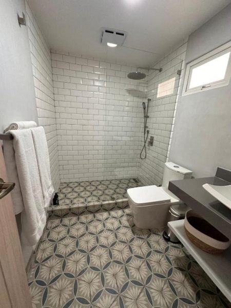 Baño moderno con ducha de lluvia y suelo hidráulico decorativo en La Riviera Hotel