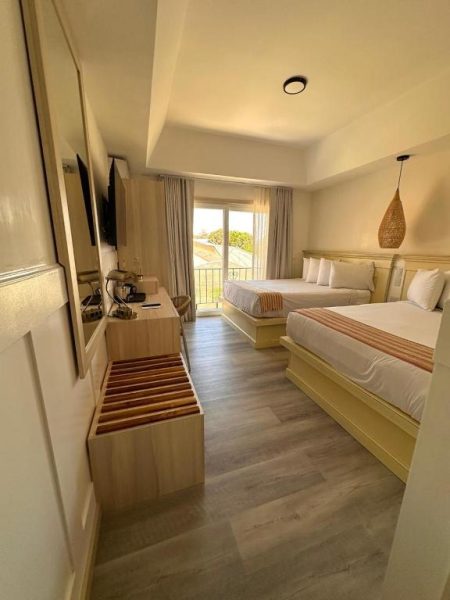 Habitación doble con dos camas y balcón con vistas en La Riviera Hotel, suelos de madera y decoración moderna