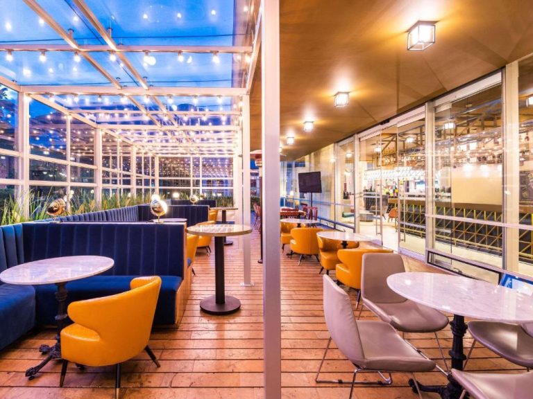 Terraza bar lounge con sofás azules y sillas amarillas del ibis Bogotá Museo con iluminación nocturna