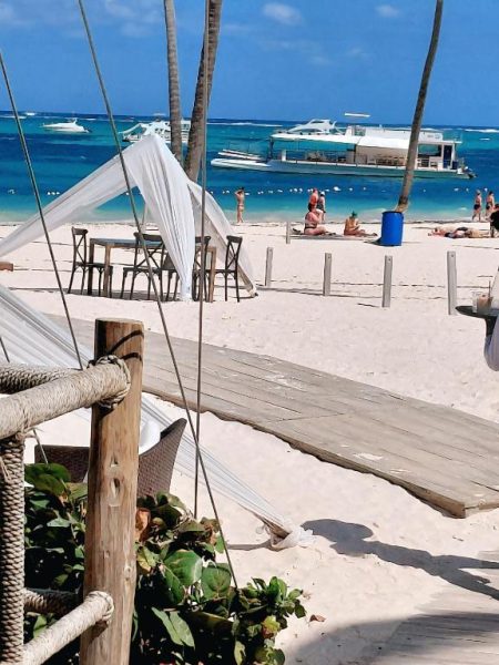 Playa de arena blanca con terraza de madera y veleros en el Hotel Punta Cana Coral Beach Area I