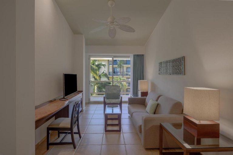 Sala de estar luminosa con sofá, TV y balcón con vistas a palmeras en Catalonia Riviera Maya Resort & Spa