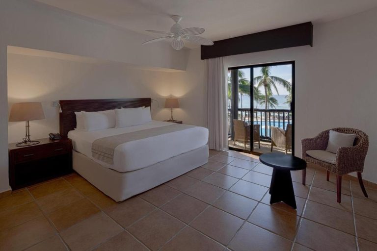 Habitación deluxe con cama king y balcón con vista a la piscina y palmeras en Catalonia Riviera Maya Resort