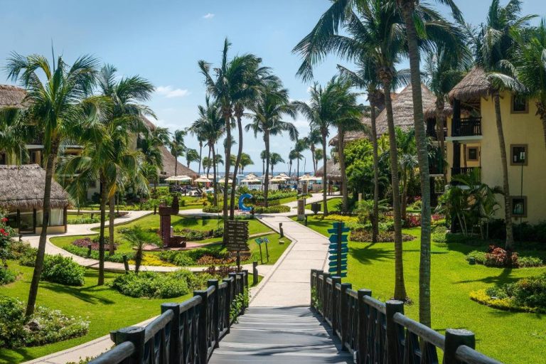 Jardines tropicales con palmeras y pasarela de acceso a la playa en Catalonia Riviera Maya Resort & Spa