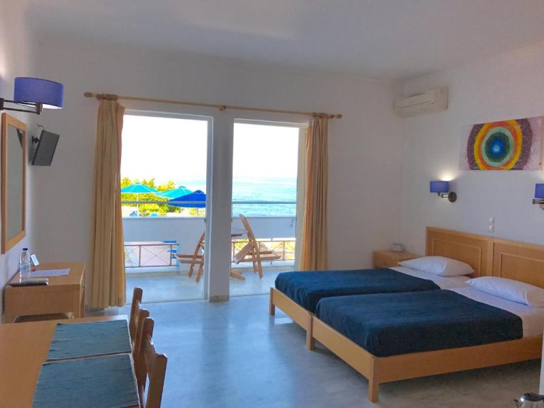 Habitación doble con camas azules y balcón con vistas al mar en Kanakis Blue Beach Apartments
